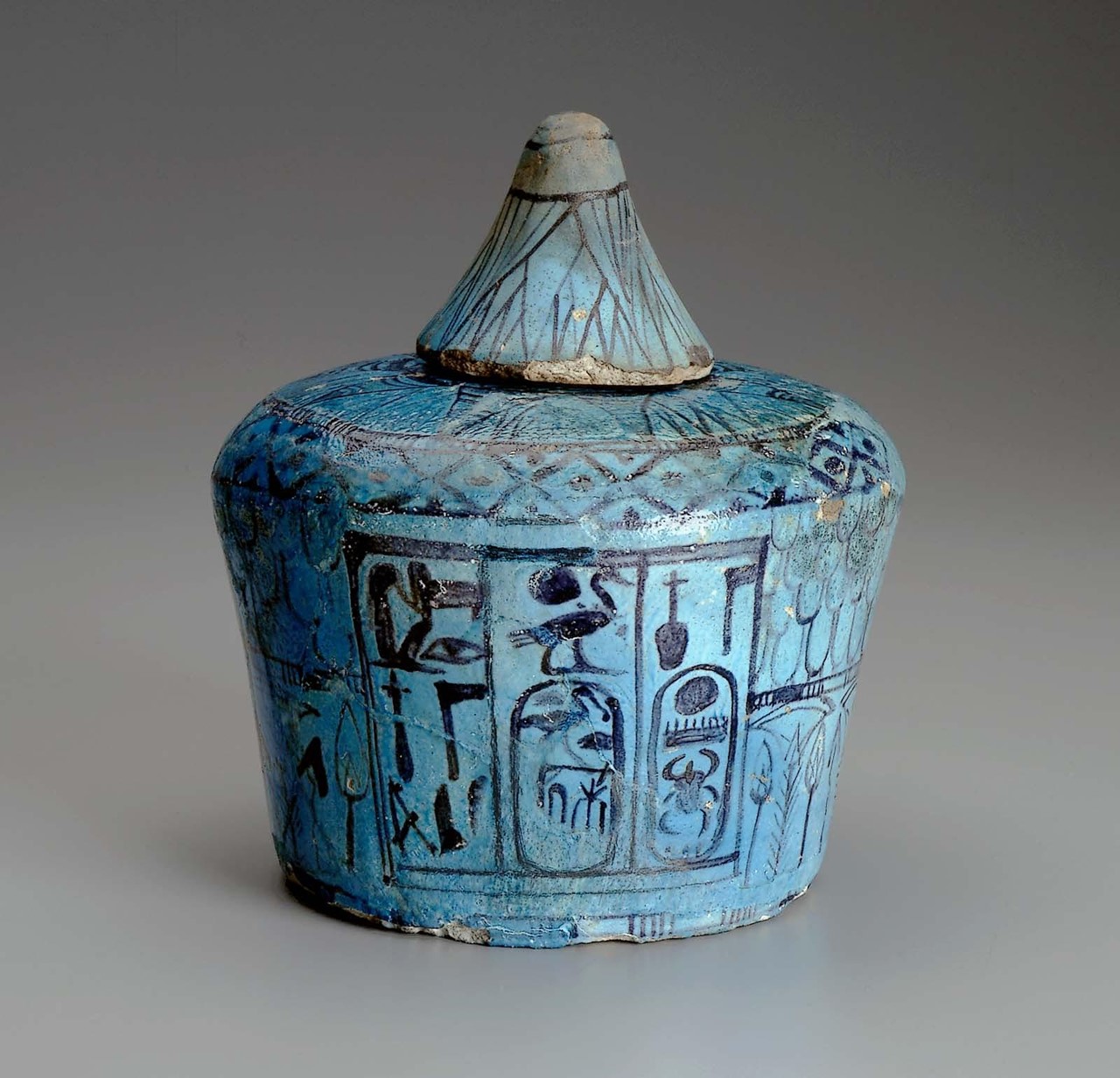Blue faience funerary vessel (with lid) from the tomb of Thutmose IV. The border of scale patterns and lotus, as well as the text, are painted in deep violet manganese pigment. https://collections.mfa.org/objects/104/ritual-vessel-nemsetjar-with-lid